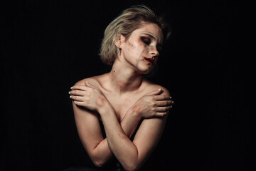 Portrait of a girl on a black background. A girl with smeared makeup hugs herself.