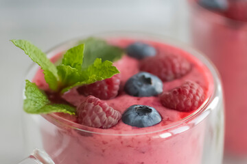 Berry smoothies in glass cups and blueberries and raspberries on a light background.