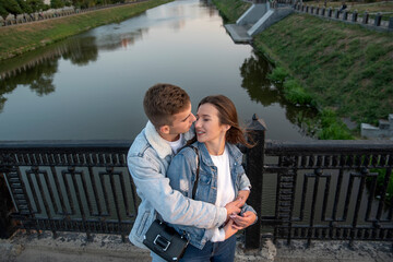 Happy couple embraces on the bridge. Guy hugs and kisses his beloved on river background. Above view. Romantic date