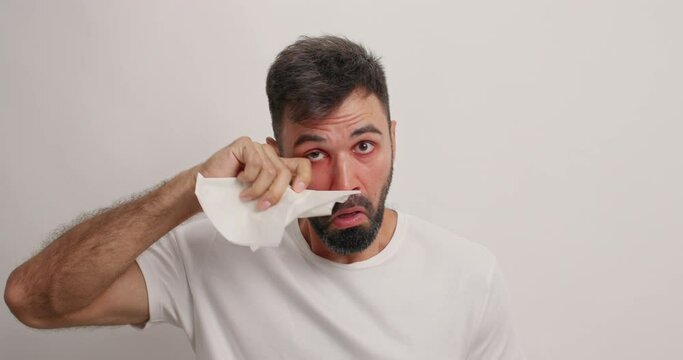 Bearded adult man blows nose in tissue suffers from allergic rhinitis uses nasal aerosol dressed casually isolated over white background. Medicines for treatment. Male model sneezes constantly