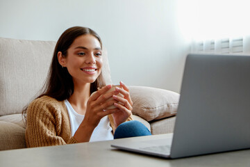 Young beautiful woman sitting alone at home and enjoying alone time with her laptop. Portrait of female sitting on the floor and watching shows on a streaming service. Close up, copy space, background
