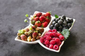 A mixture of fresh berries in a white plate on a dark gray background