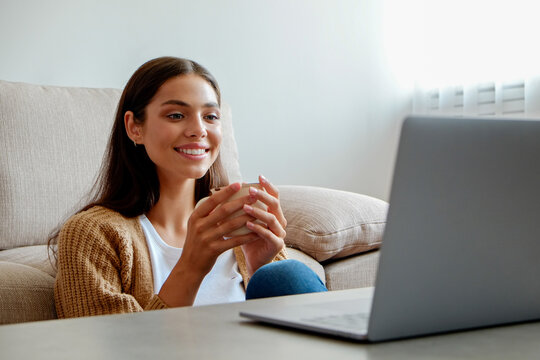 Young beautiful woman sitting alone at home and enjoying alone time with her laptop. Portrait of female sitting on the floor and watching shows on a streaming service. Close up, copy space, background