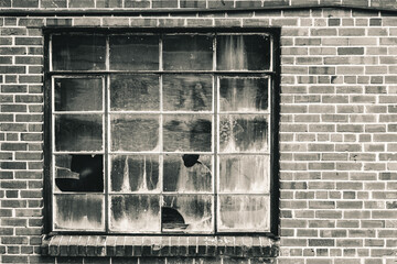 Old window with broken panes that has been boarded up. Set in brick wall in warm tone black and...