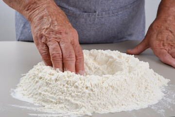 Female hands of an elderly woman knead the dough on a gray table. Senior woman in a gray apron preparation of dough for a pizza, bread, pasta, festive cake. Selective focus