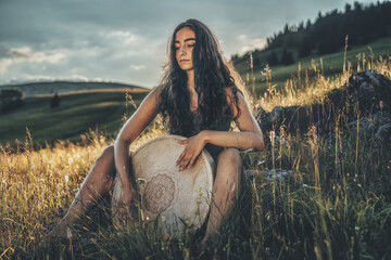 beautiful shamanic girl playing on shaman frame drum in the nature.