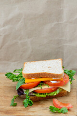 Sandwich with tomatoes, cheese and arugula on a wooden tray, on a craft paper background. Vertical photo. Place for your text.