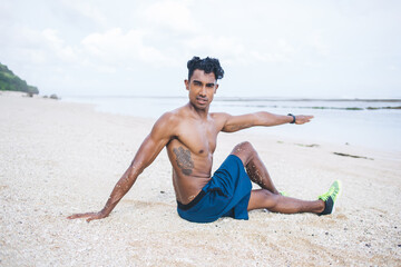 Ethnic man in shorts doing sport exercises at beach