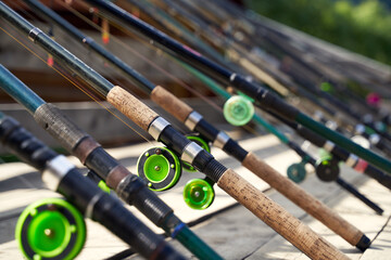 Many fishing rods on the wooden pier by the river or lake on a sunny day