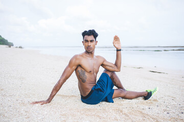 Ethnic man doing yoga exercise at sand beach