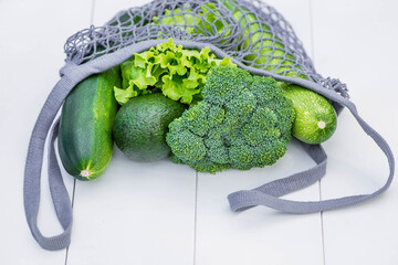 A string bag with green vegetables in close-up on a white wooden background. Healthy, dietary food...
