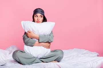 Photo of shiny adorable young woman nightwear sitting duvet hugging pillow looking empty space isolated pink color background