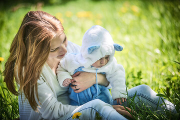 Yong's mother holding cute baby on hands in spring park. Outdoor seasonal nature with green leaves trees.