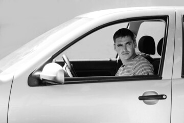 Serious stylish caucasian young man sitting in car. 20s guy driver. Silver gray car. Attractive brunette men in vehicle. Buyer or auto dealer concept. First owner. Black and white