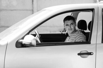 Serious stylish caucasian young man sitting in car. 20s guy driver. Silver gray car. Attractive brunette men in vehicle. Buyer or auto dealer concept. First owner. Black and white. Handsome style