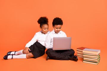 Full size photo of two young afro school kids classmates make homework computer isolated over orange color background