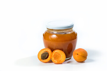 Apricot jam in a jar with apricots whole and in half over white background.