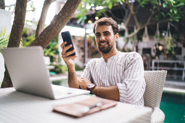 Young happy man with smartphone at table with laptop