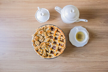 Decorated apple pie on a wooden table and a tea pot and cup of tea. Afternoon tea concept.
