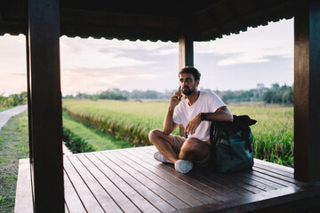 Male tourist talking on smartphone while relaxing near green field