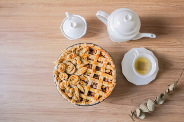 Decorated apple pie on a wooden table and a tea pot and cup of tea. Afternoon tea concept.