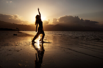 Beautiful woman dancing by the sea at sunset
