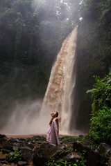 Beautiful woman in a pink dress near a waterfall in Bali