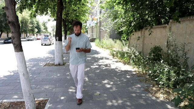 a man walks on the sidewalk and reads the news on his smartphone while waiting for a taxi ride