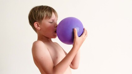 A boy tries to inflate a purple balloon on a white background. Funny situation