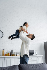 cheerful asian father holding in arms toddler girl at home