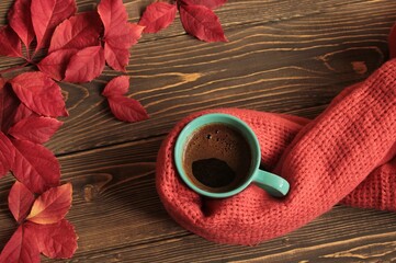 Coffee in a blue mug, wrapped in a scarf and red leaves.