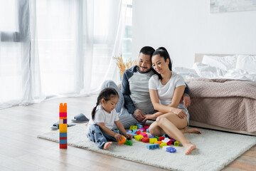 cheerful asian parents looking at toddler daughter playing building blocks