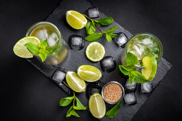 Cold mojito cocktail on the slate board with black background. Refreshing a tasty summer drink full of mint and lime.