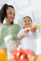 low angle view of asian mother looking at happy daughter preparing salad in kitchen