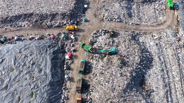 Aerial top view of A Huge Waste, garbage, dump, rubbish landfill. A landfill compactor, group of workers sort out the garbage in the landfill. Trash trucks dump waste polluting products.