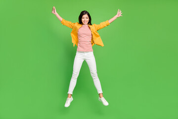 Fototapeta na wymiar Full length photo of cute brown hairdo young lady jump wear shirt trousers sneakers isolated on green color background