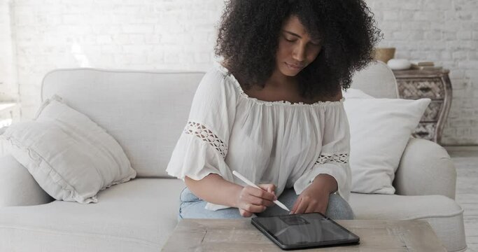 Mixed race female freelance artist using digital tablet with electronic pencil to create crypto art or drawing illustrations. Designer working home, sketching in graphic notepad. Learning technologies