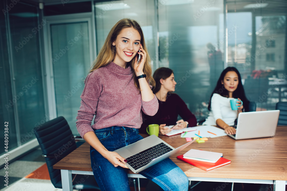 Poster portrait of cheerful female programmer with laptop computer smiling at camera during brainstorming m