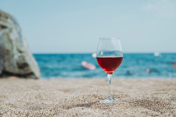  Glass of red wine against the background of the Mediterranean beach and the sea in a tourist town in the summer under sunlight. Summer, travel, lifestyle, relaxation, and enjoyment concept.