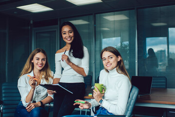 Group of cheerful Asian and Caucasian female colleagues smiling at camera during work brainstorming in office interior, successful partners spending meeting time for collaborate on ideas for startup