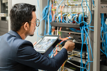 Stock photo of a young network technician holding tablet working to connecting network cables in...