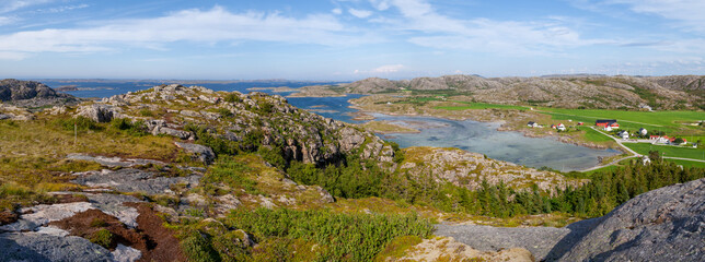 Naklejka na ściany i meble Wide panorama view from above of a rock cliff and the ocean, green valley and small village in Norway. Valoy. Vikna Green grass around.
