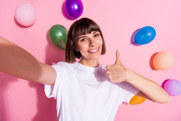 Self-portrait of attractive trendy cheerful girl showing thumbup decor air balls flying isolated over pink pastel color background