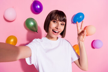 Self-portrait of attractive cheerful girl showing v-sign having fun air balls flying isolated over...