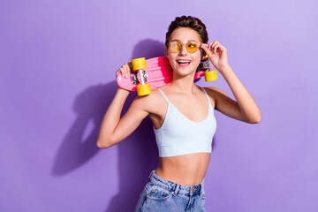 Photo portrait girl wearing sunglass blue jeans keeping long board laughing dreamy isolated pastel violet color background