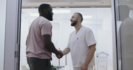 In the dental clinic a male  African American patient is shaking hands with a male medical worker.
