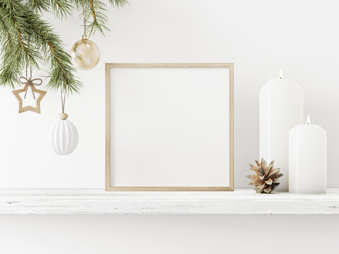 Small square wooden frame mockup with hanging pine branch, pinecone and candles on shelf on empty white wall background. Minimal Christmas interior decoration. 3d rendering, illustration