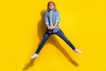 Photo of funny charming young gentleman wear jeans shirt dark glasses jumping high smiling isolated yellow color background