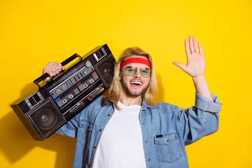 Zelfklevend Fotobehang Photo of funky pretty young guy dressed denim shirt smiling waving arm palm holding boom box isolated yellow color background © deagreez
