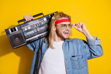Photo of cool sweet gentleman wear jeans shirt arm glasses listening boombox looking empty space smiling isolated yellow color background